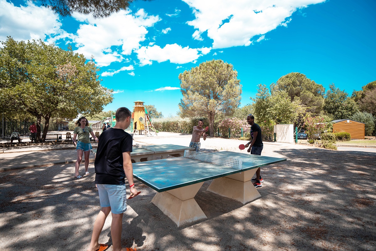 People playing table tennis outdoors surrounded by trees and play structures at Les Albères