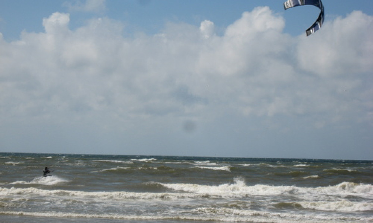 At Dancamps Nordsø, a kite surfer is soaring above turbulent waves beneath a partly cloudy sky.