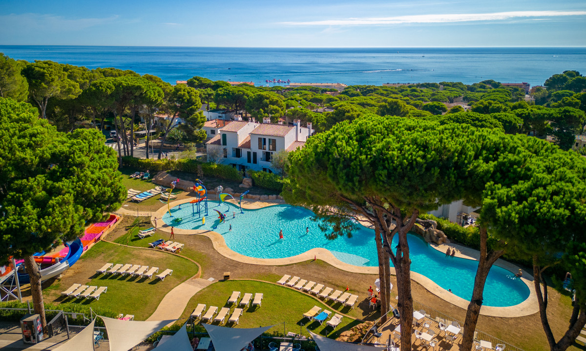Swimming pool with people enjoying water activities, surrounded by loungers and trees, overlooking the sea at Interpals Eco Resort
