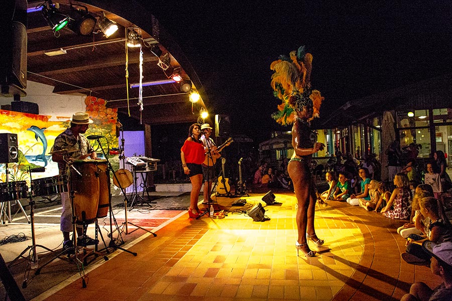 Musicians performing and a dancer in feathered costume entertaining audience seated around stage at night at Belvedere Pineta