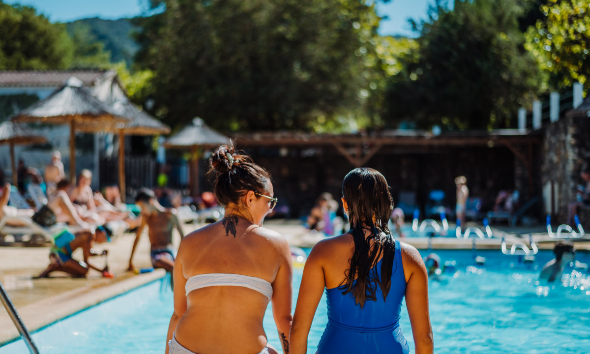 At La Clémentine, two individuals relax by the pool, encircled by sunbathers and swimmers, beneath the radiant sunlight.