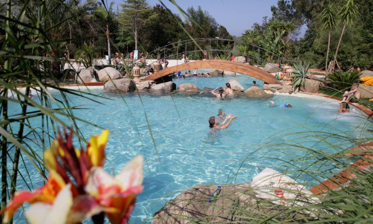 At Ultima Spiaggia, individuals swim and unwind in a pristine, open-air pool with a charming wooden bridge nearby.