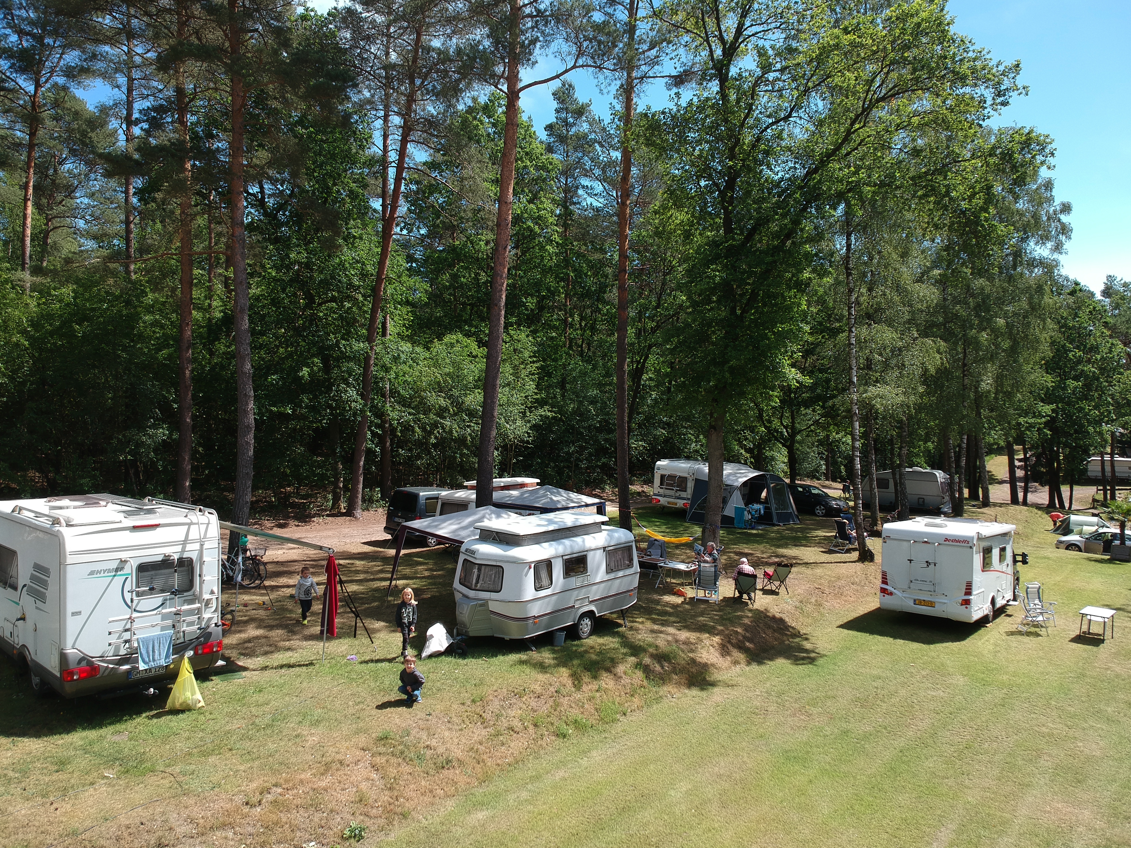 At Sonnenberg, caravans are stationed beneath towering trees while individuals unwind and children frolic on the grassy expanse.