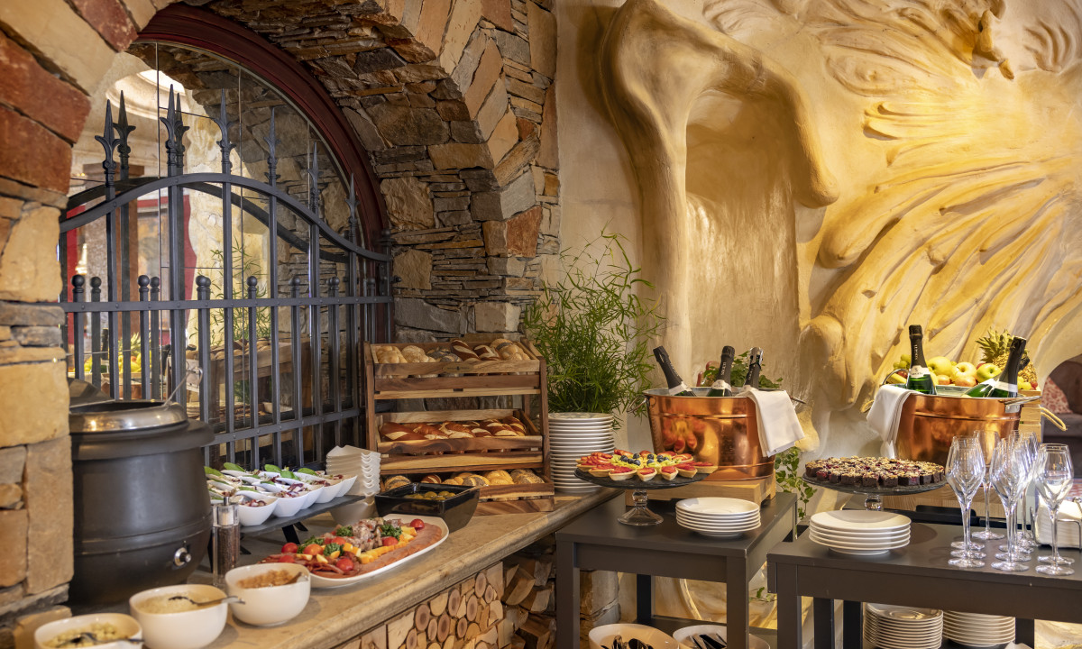 Food buffet displaying breads, fruits, and champagne in a rustic setting with stone walls and artistic decor at Kesselspitze Valamar Collection Hotel