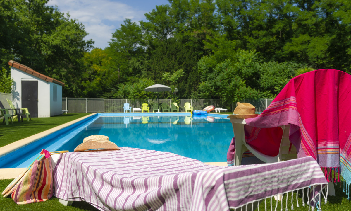 At Coucou, there are lounge chairs with towels positioned near a swimming pool, encircled by trees and additional lawn chairs.