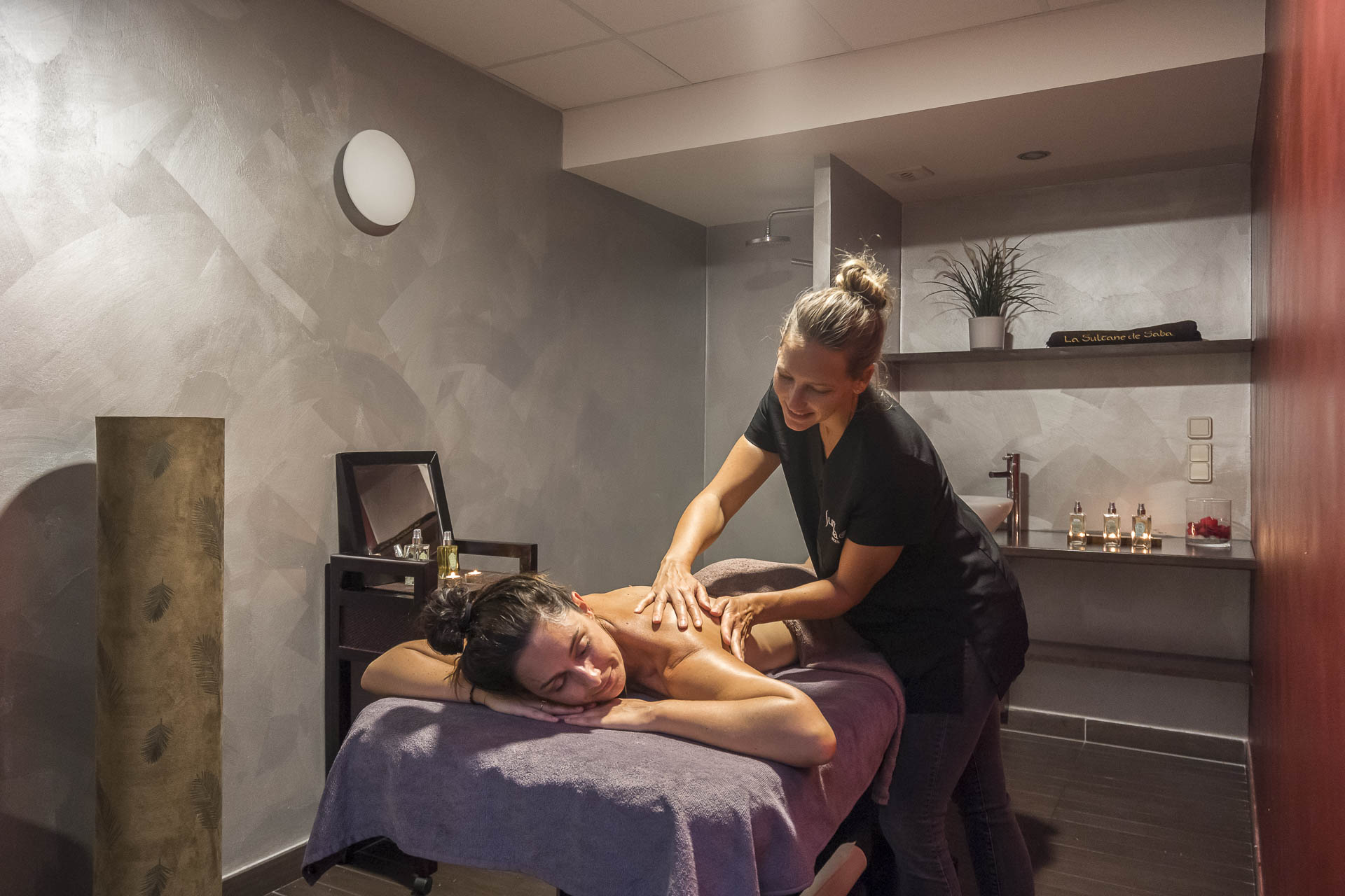 Massage therapist performing massage on a relaxed client in a serene, dimly lit spa room with modern decor at Escale St. Gilles