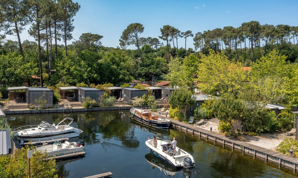 Boat navigating a narrow canal with modern cabins lining the wooded shoreline at Maguide
