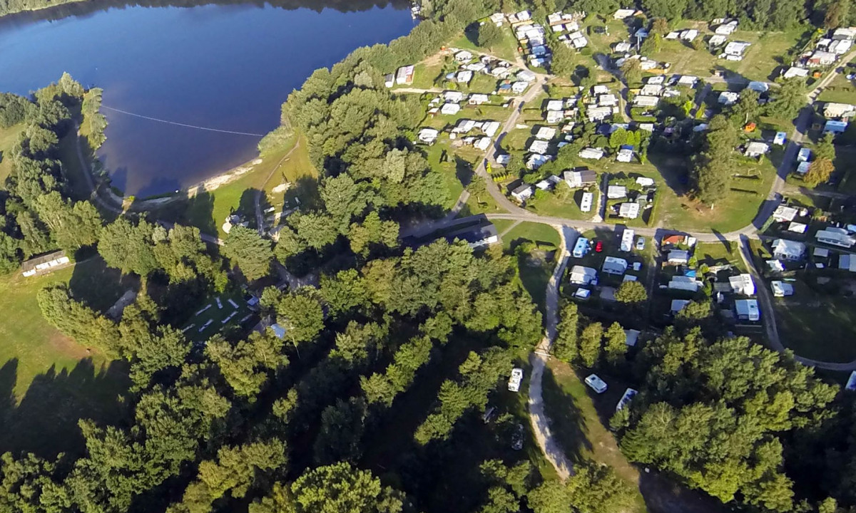 At KNAUS Campingpark Oyten, an overhead perspective reveals a lakeside camping area filled with various trailers nestled within a wooded region.