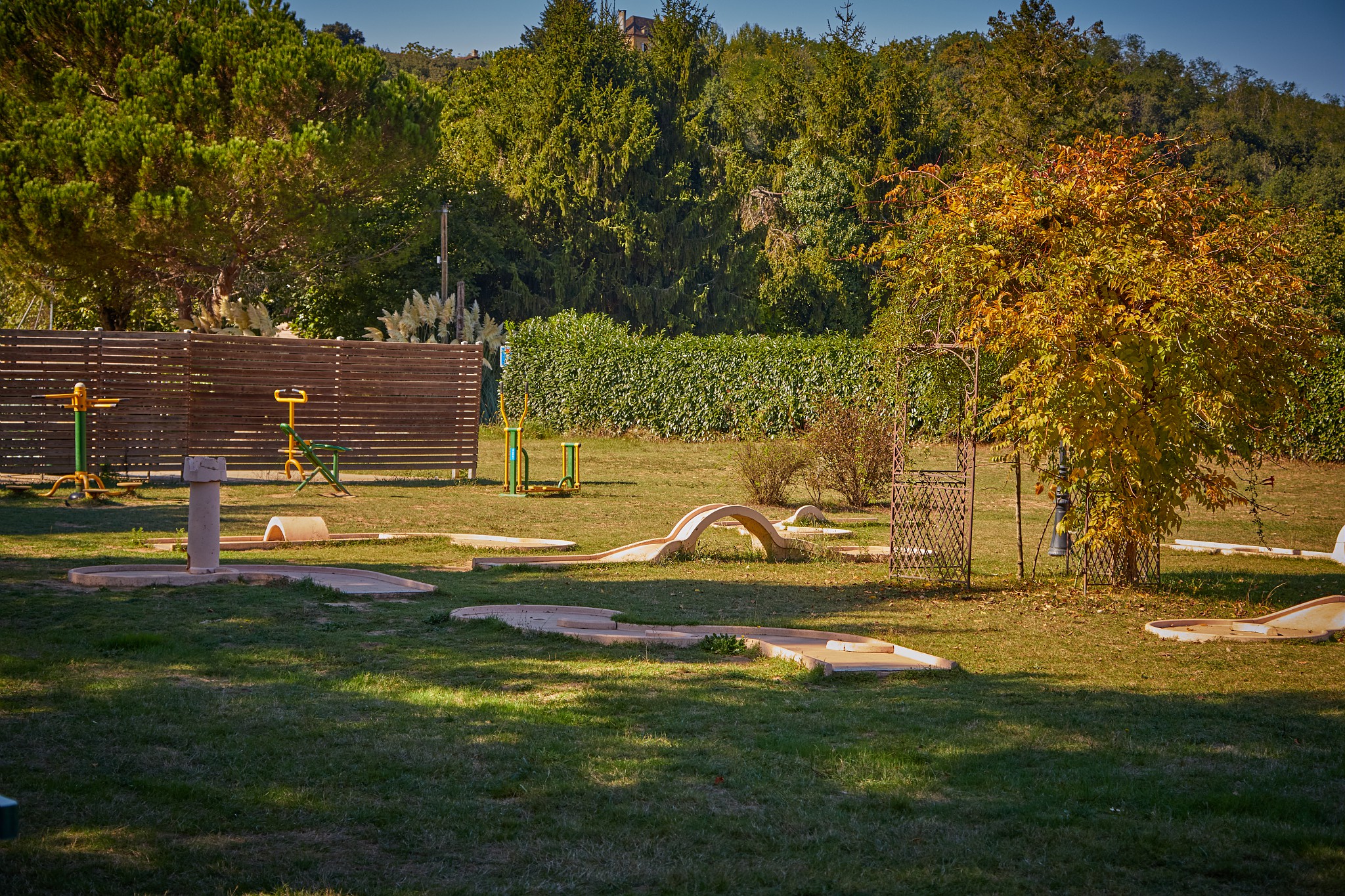 At Marvilla Parks Domaine de Soleil Plage, there is a mini-golf course featuring obstacles situated on grassy land, encircled by fitness apparatus and vibrant foliage.