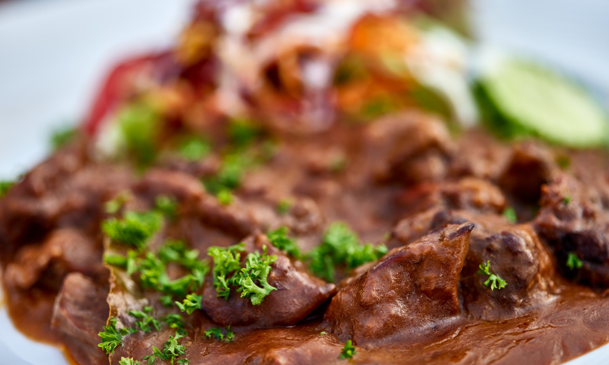 At Urban Gardens Gent, beef stew adorned with fresh parsley is presented on a plate next to a medley of mixed vegetables.