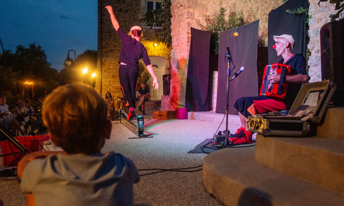 Performer on slackline balances while musician plays accordion, watched by audience at Domaine de Sévenier
