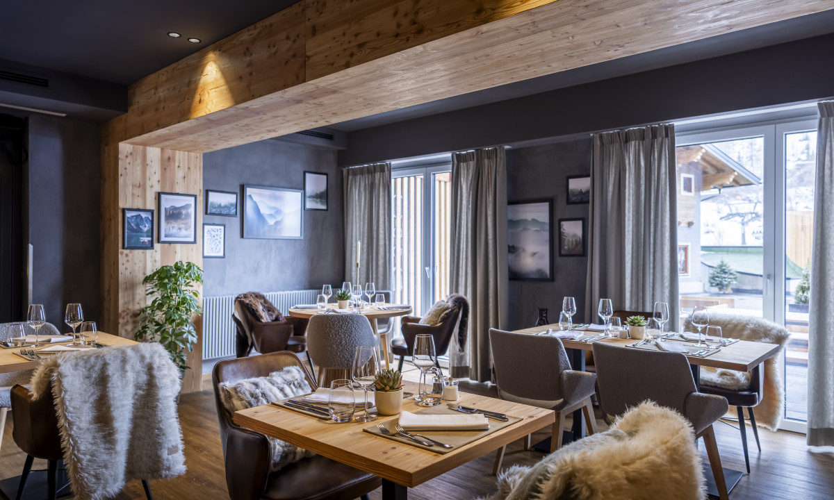 Tables set elegantly for dining, chairs adorned with soft fur, within a cozy, wood-paneled restaurant at Kesselspitze Valamar Collection Hotel