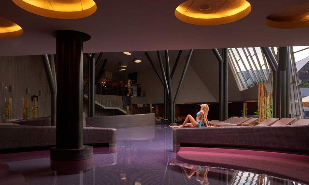 A woman in a swimsuit relaxes on a lounge chair in a modern indoor pool area with unique architecture at Hotel Sotelia