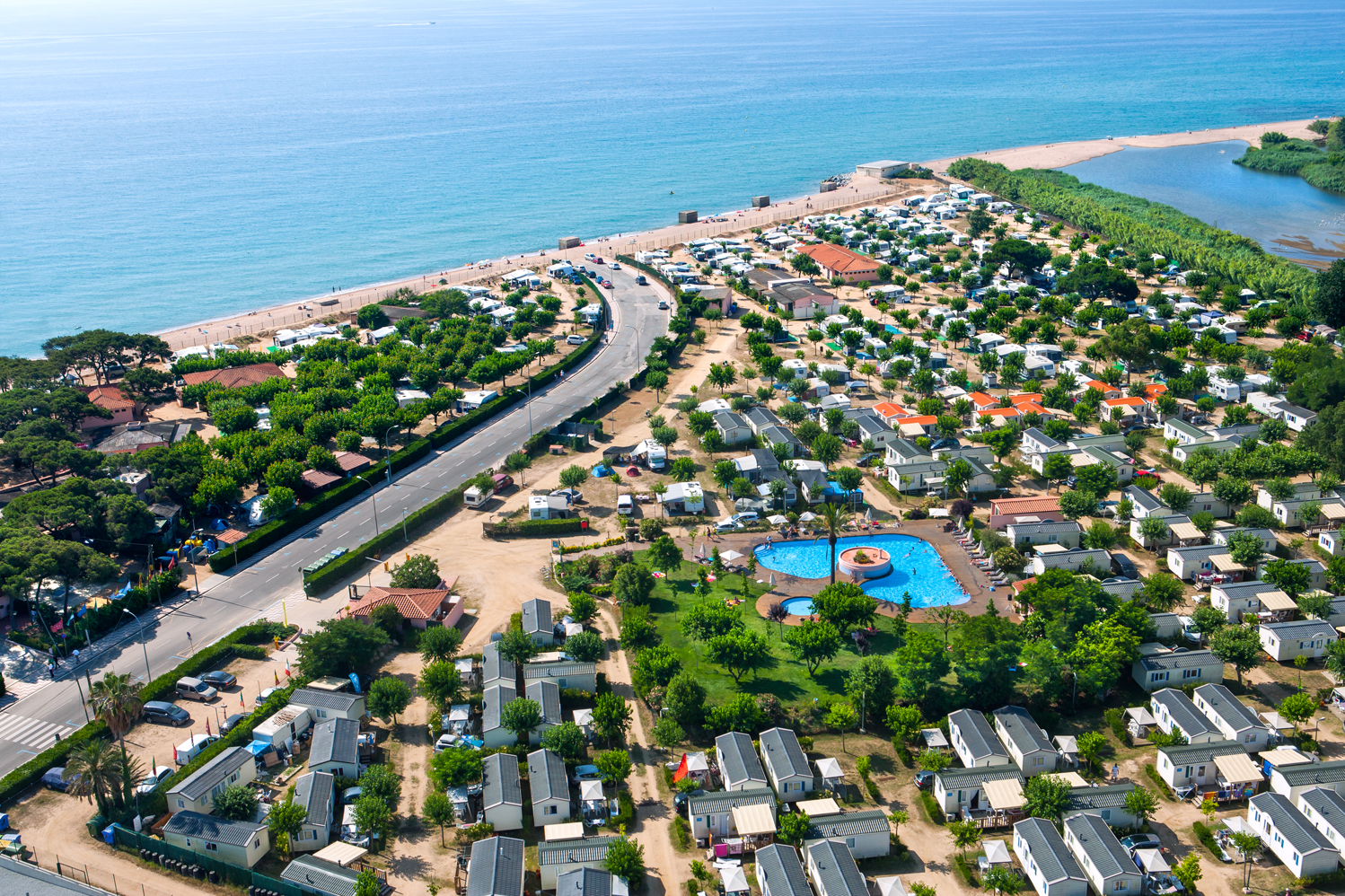Aerial view of a beachside campsite with mobile homes, a road, a pool, and the ocean in the background at El Pinar