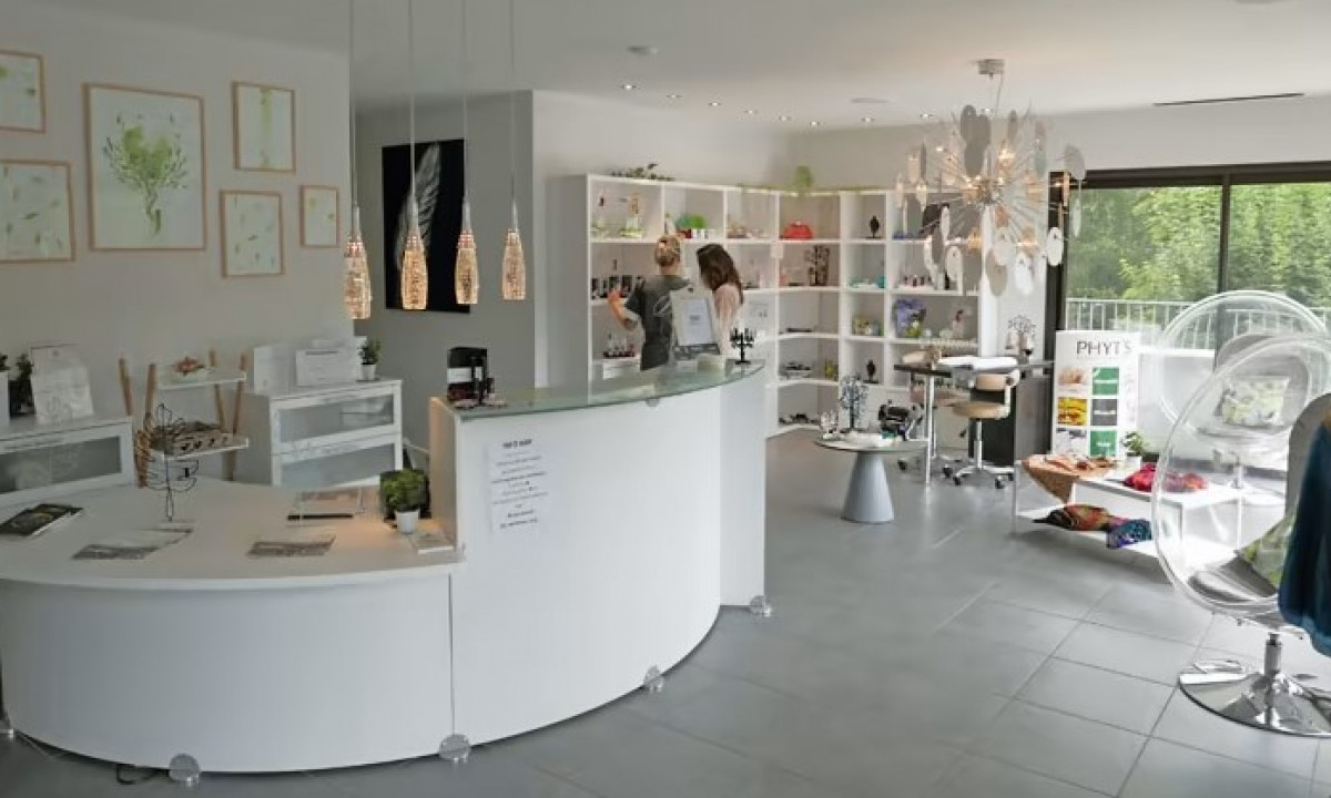 At Les Ranchisses, there is a curved white reception counter adorned with decorative pieces, a glowing chandelier, and shelves filled with merchandise.