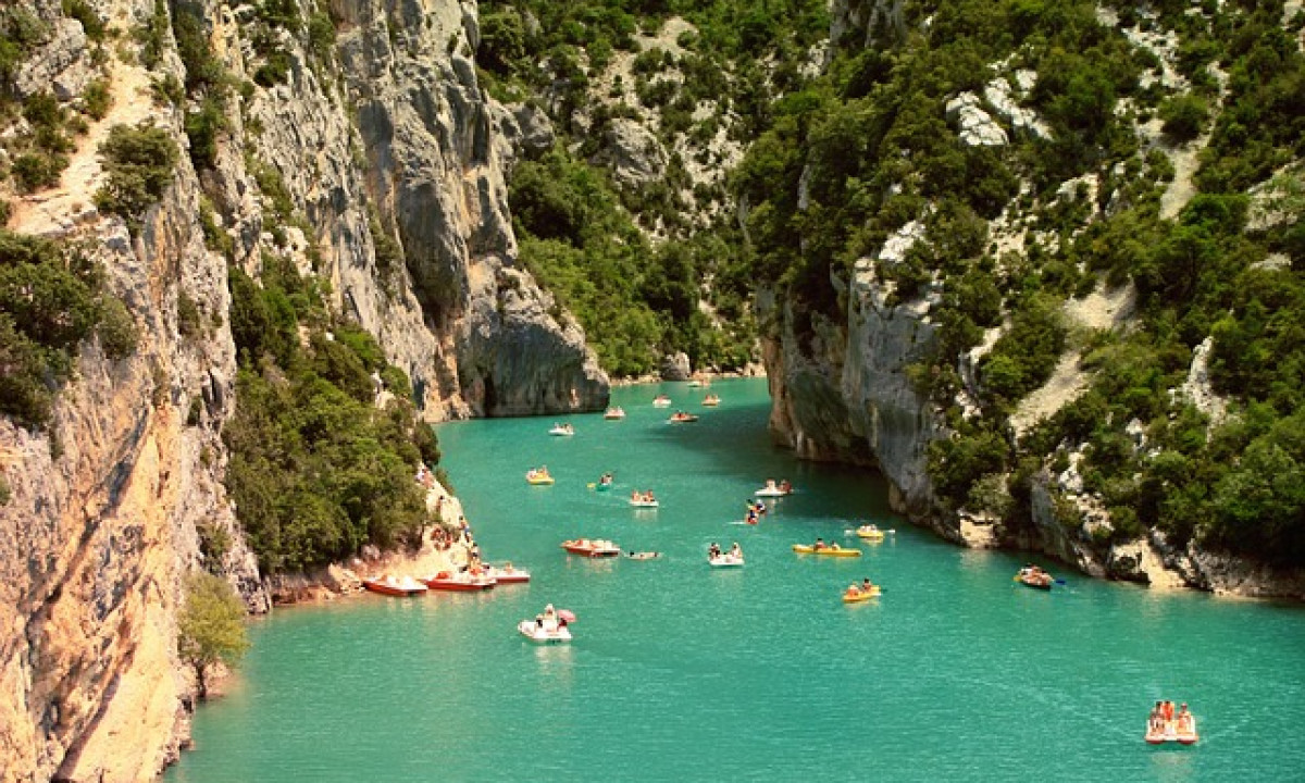 At La Clémentine, vessels drift in azure waters amidst verdant, towering cliffs enveloped by foliage.