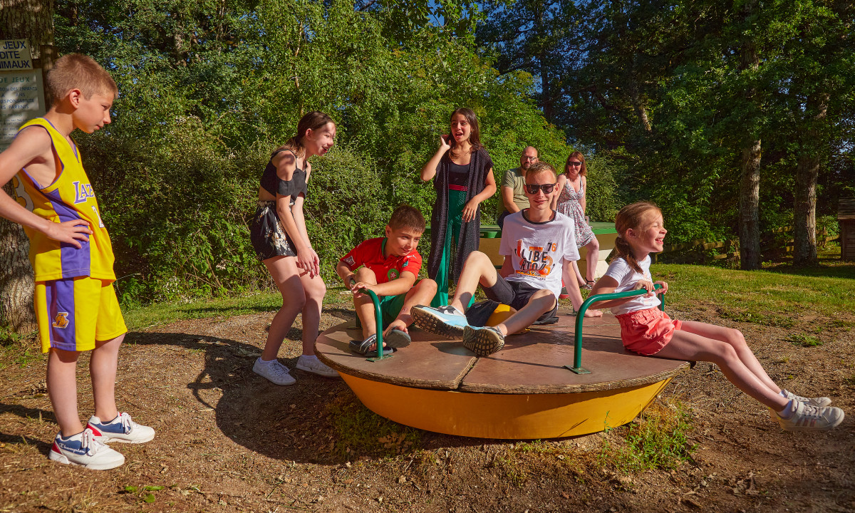 At Terrasses du Lac, kids are seated and upright on a carousel, giggling and having fun, encircled by trees.