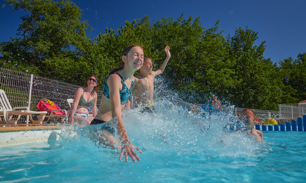 At Terrasses du Lac, kids are enjoying themselves in a pool, playfully splashing water, encircled by trees and a fence.