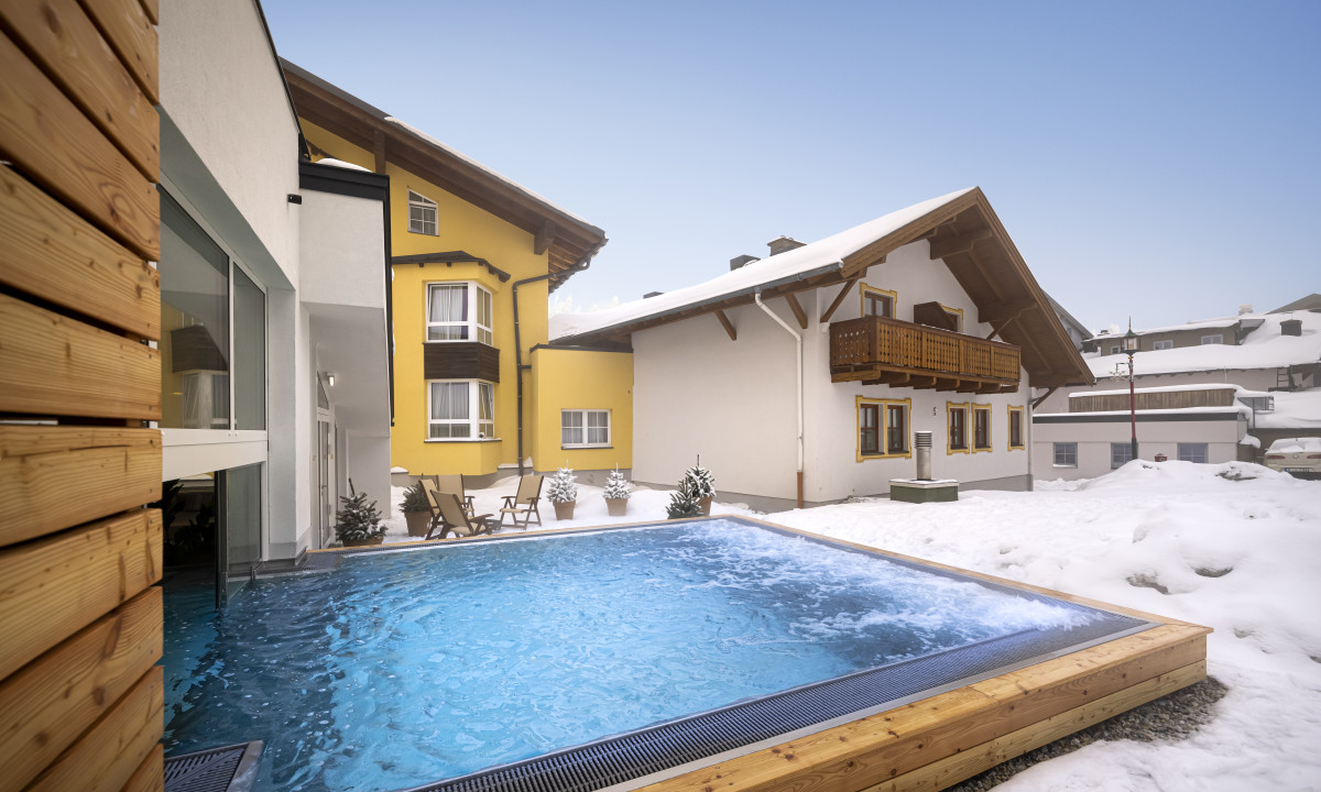 A heated outdoor pool steams in a snowy courtyard with chalet-style buildings at Valamar Obertauern Hotel