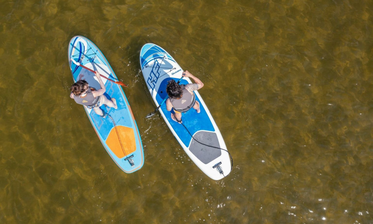 Two people paddleboarding on calm, greenish water with clear skies overhead at Maguide