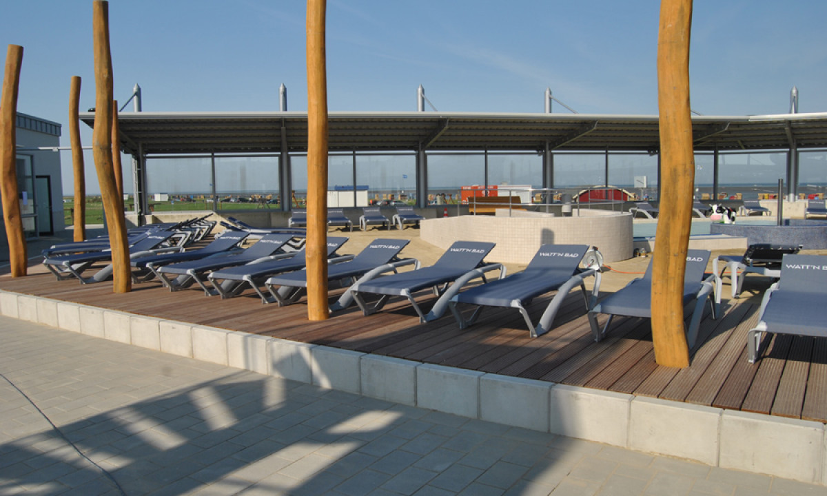 At KNAUS Campingpark Dorum, sunbeds are positioned on a timber terrace with a contemporary pavilion in the backdrop.