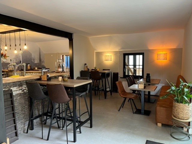 At de Vinkenkamp, tables and chairs are positioned in a snug dining space featuring a contemporary bar arrangement, with a warmly illuminated interior.