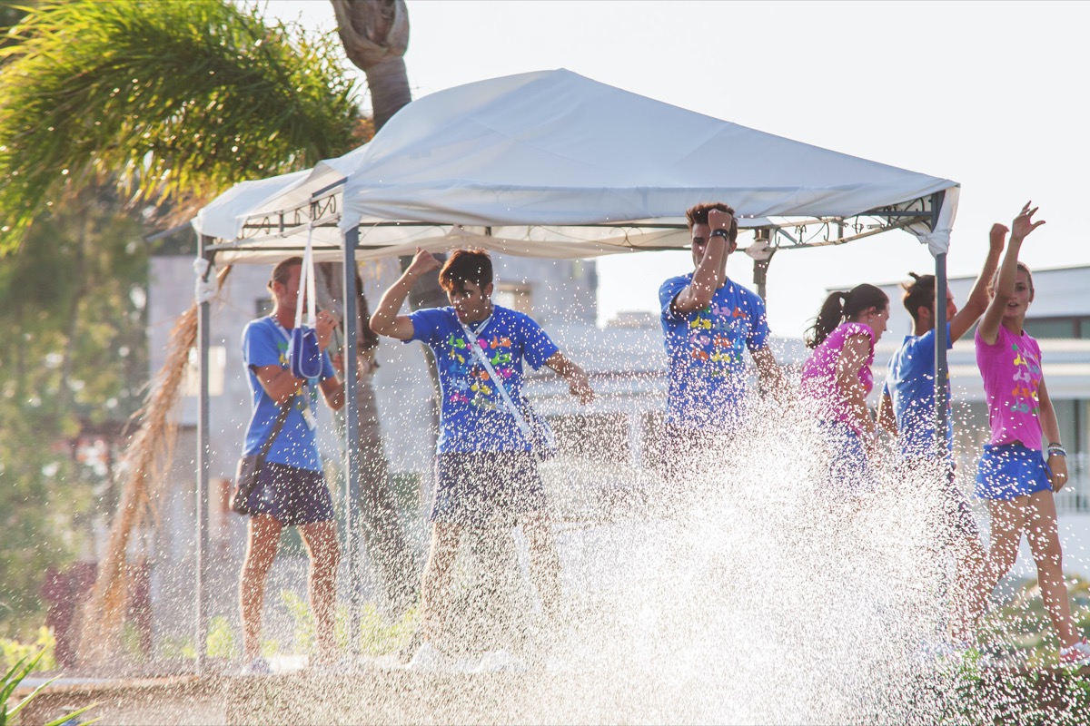 Group of young people dancing under a canopy while water splashes around them at I Turchesi Club Village