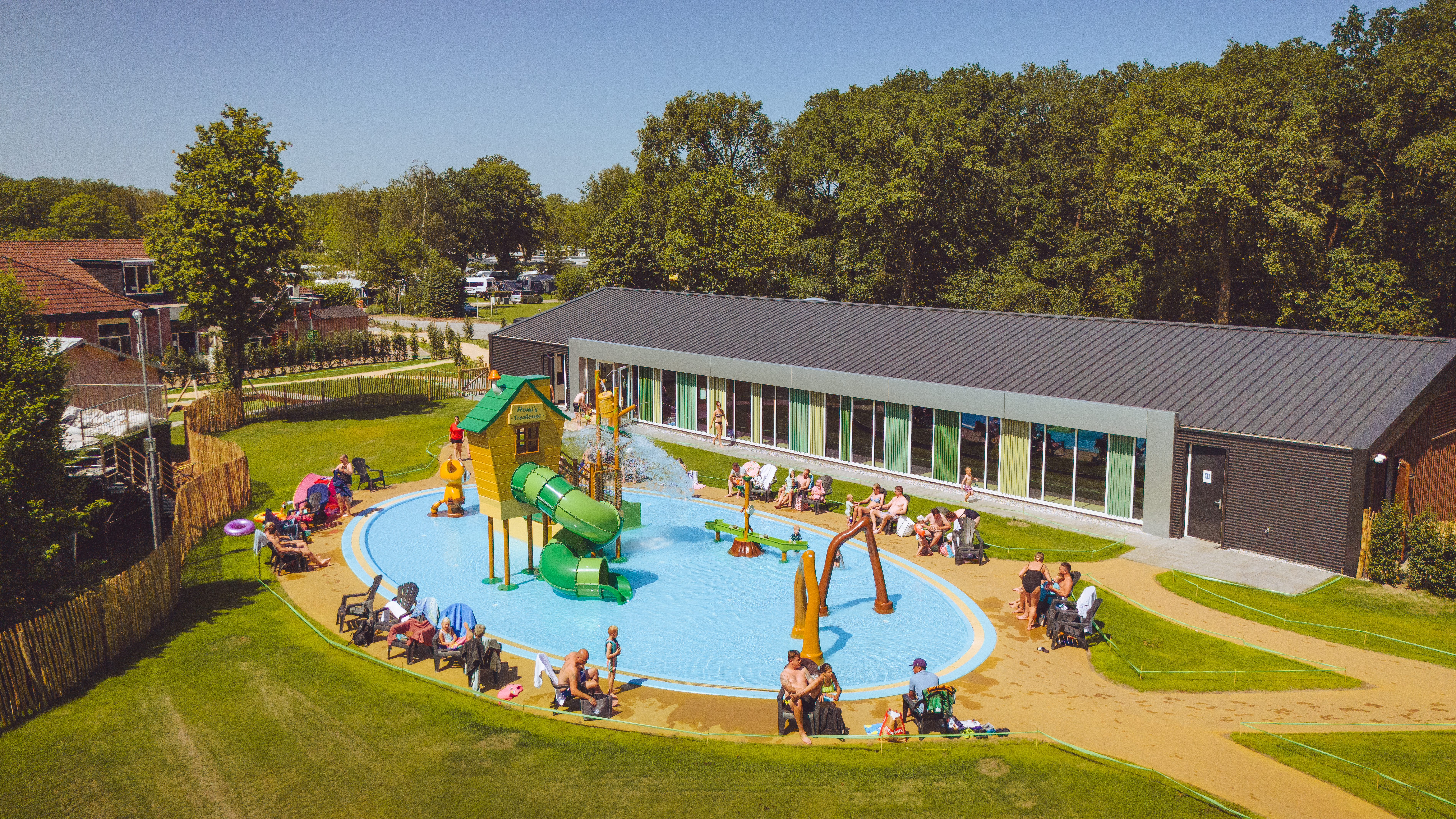 Children playing in a colorful splash pad featuring slides and sprinklers, surrounded by sunbathers and greenery at Marvilla Parks Kaatsheuvel