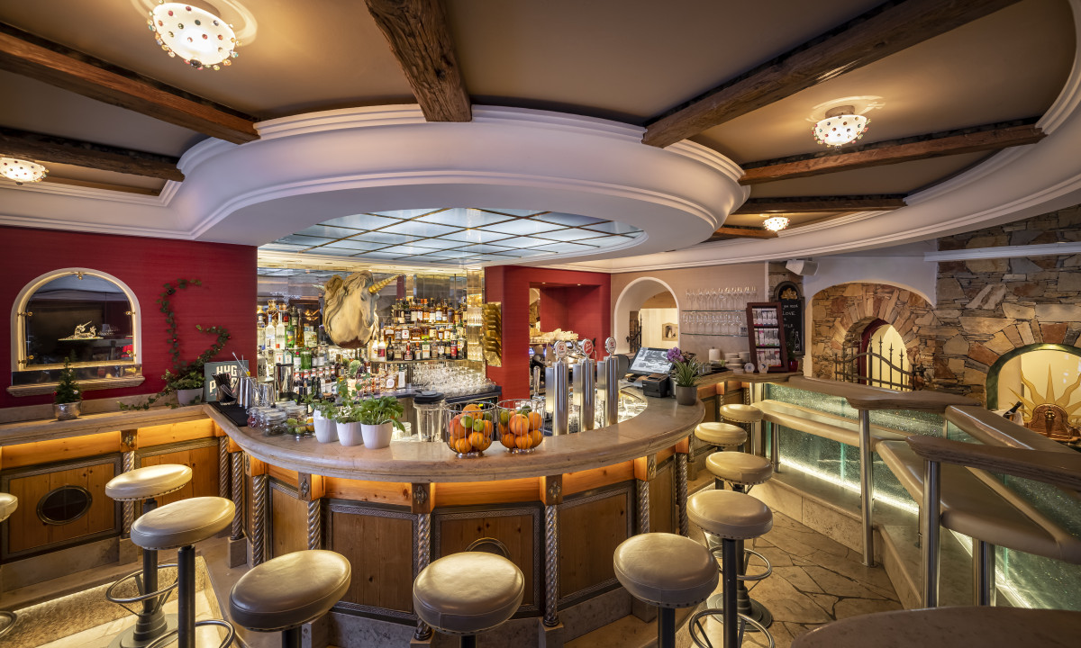 Circular bar with stools, decorated ceiling, and stocked shelves; cozy, rustic interior with warm lighting at Kesselspitze Valamar Collection Hotel