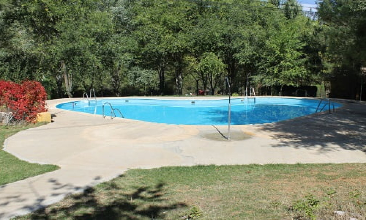 At Puente de las Herrerías, a pool mirrors sunlight, encircled by trees and a grassy area.