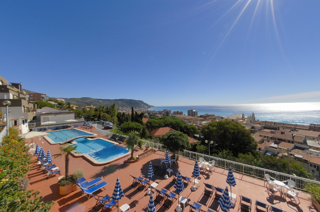 Swimming pool area with sun loungers and umbrellas overlooking a coastal city and the ocean at Sant' Anna Residence