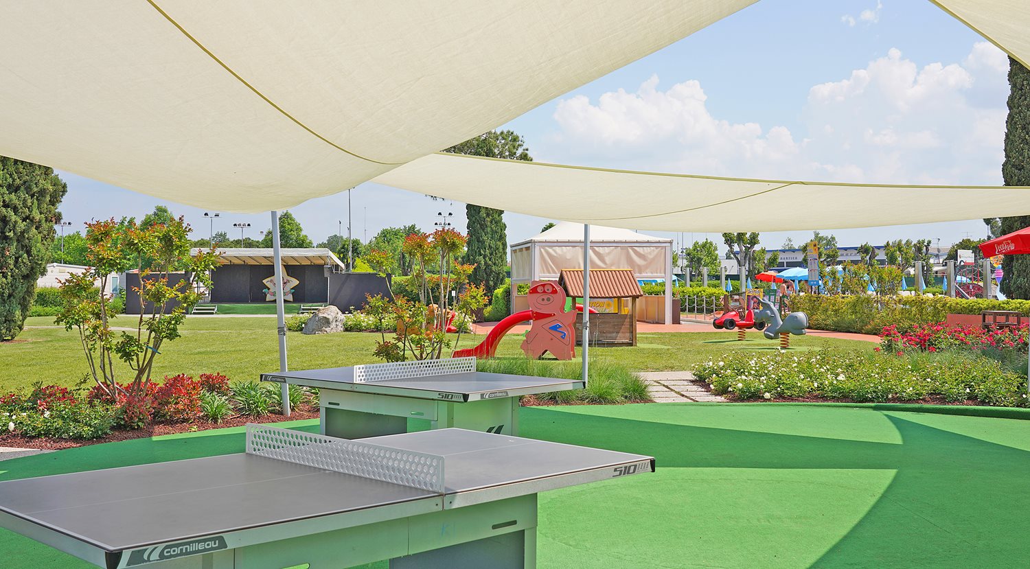 Table tennis table under sunshade with playground in background amidst manicured garden and lawn at San Francesco