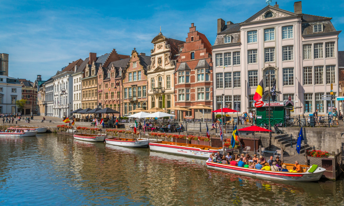 At Urban Gardens Gent, vessels transporting visitors glide along a waterway, framed by vibrant historic structures and al fresco dining spots.