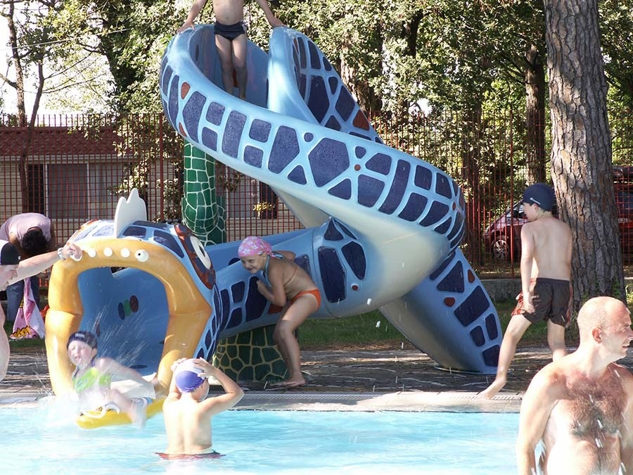 Children play on a blue animal-themed water slide beside a swimming pool surrounded by trees and fences at Belvedere Pineta