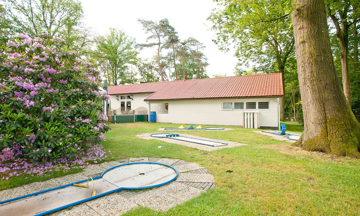 Mini-golf course surrounded by trees, with a building in the background and flower bushes nearby at de Wrange