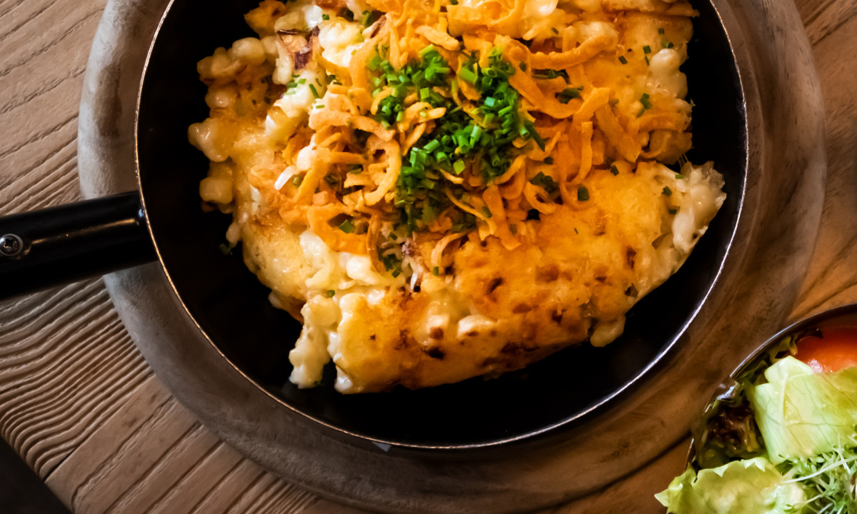 Cheesy pasta topped with chives in a pan, accompanied by a fresh salad on a rustic wooden table at Valamar Obertauern Hotel