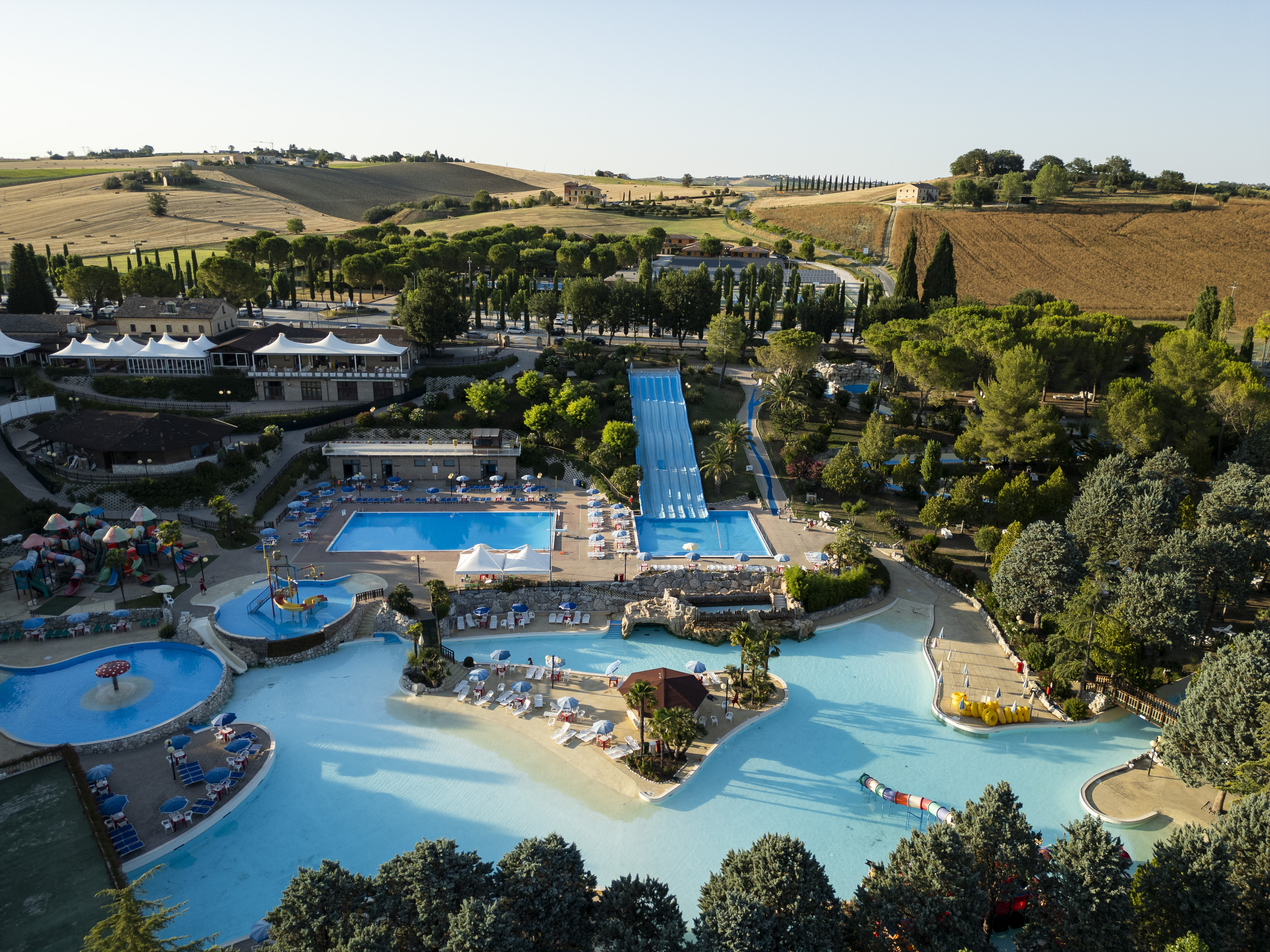 Large swimming pool complex with slides and lounge areas, surrounded by lush greenery and fields at Centro Vacanze Verde Azzurro