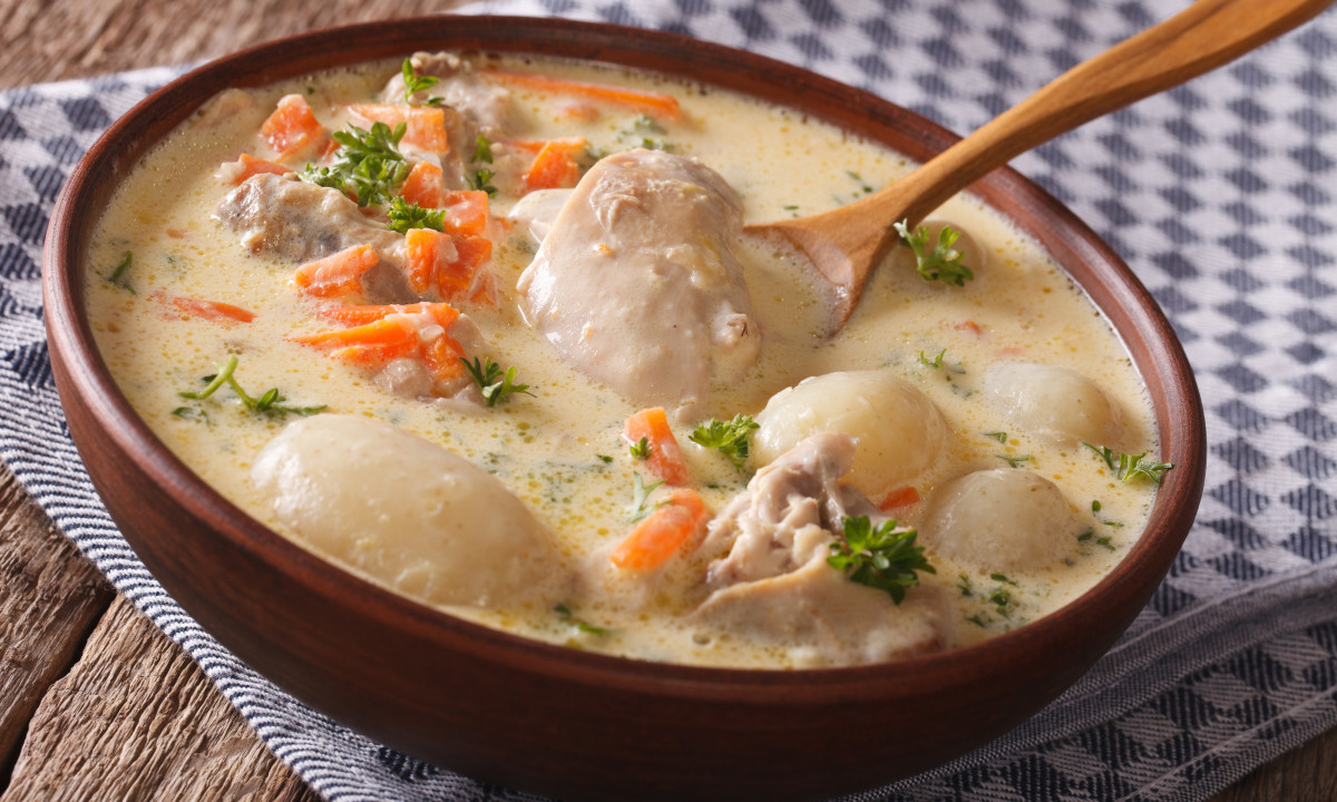 At Urban Gardens Gent, a bowl of rich stew containing chicken, vegetables, and dumplings is being mixed with a wooden spoon.