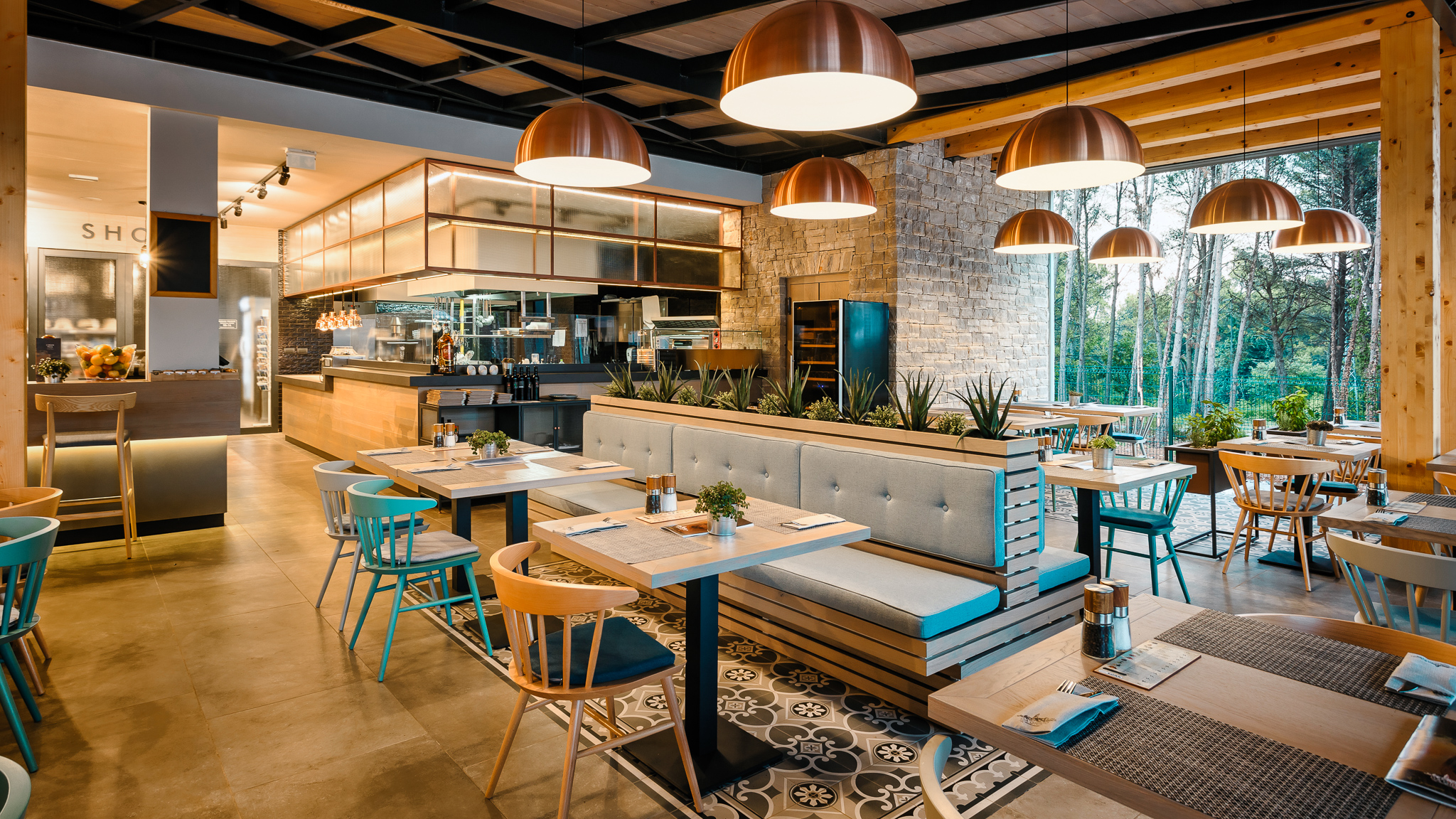 Modern restaurant with wooden furnishings illuminated by pendant lights, featuring a cozy seating area and visible kitchen at Santa Marina Boutique