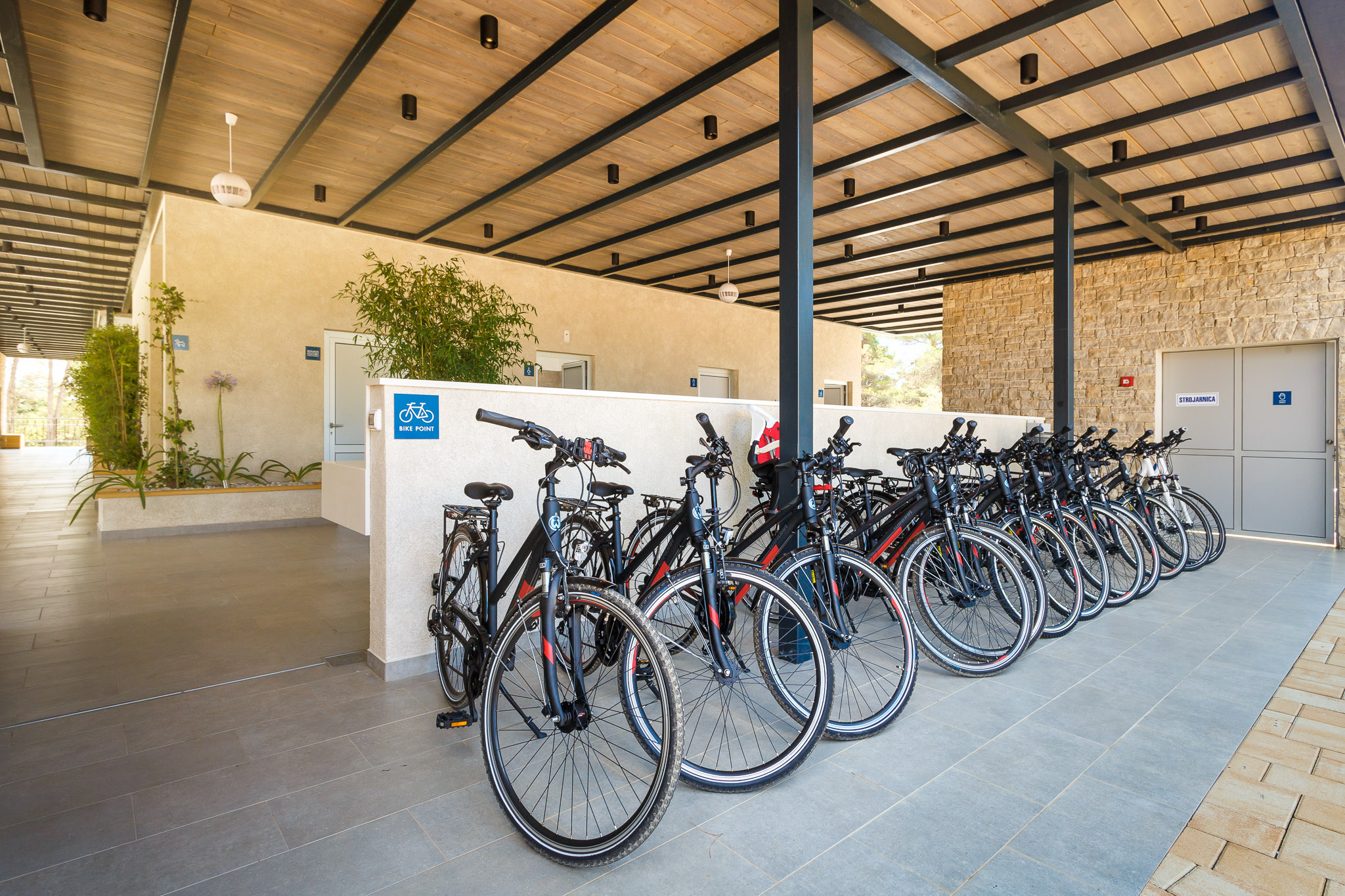 Bicycles parked in an organized line under a covered shelter with plants and walls at Santa Marina Boutique