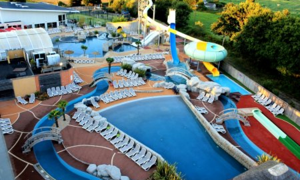 At Le Domaine de Léveno, the water park includes various pools and water slides, encircled by lounge chairs and lush vegetation.