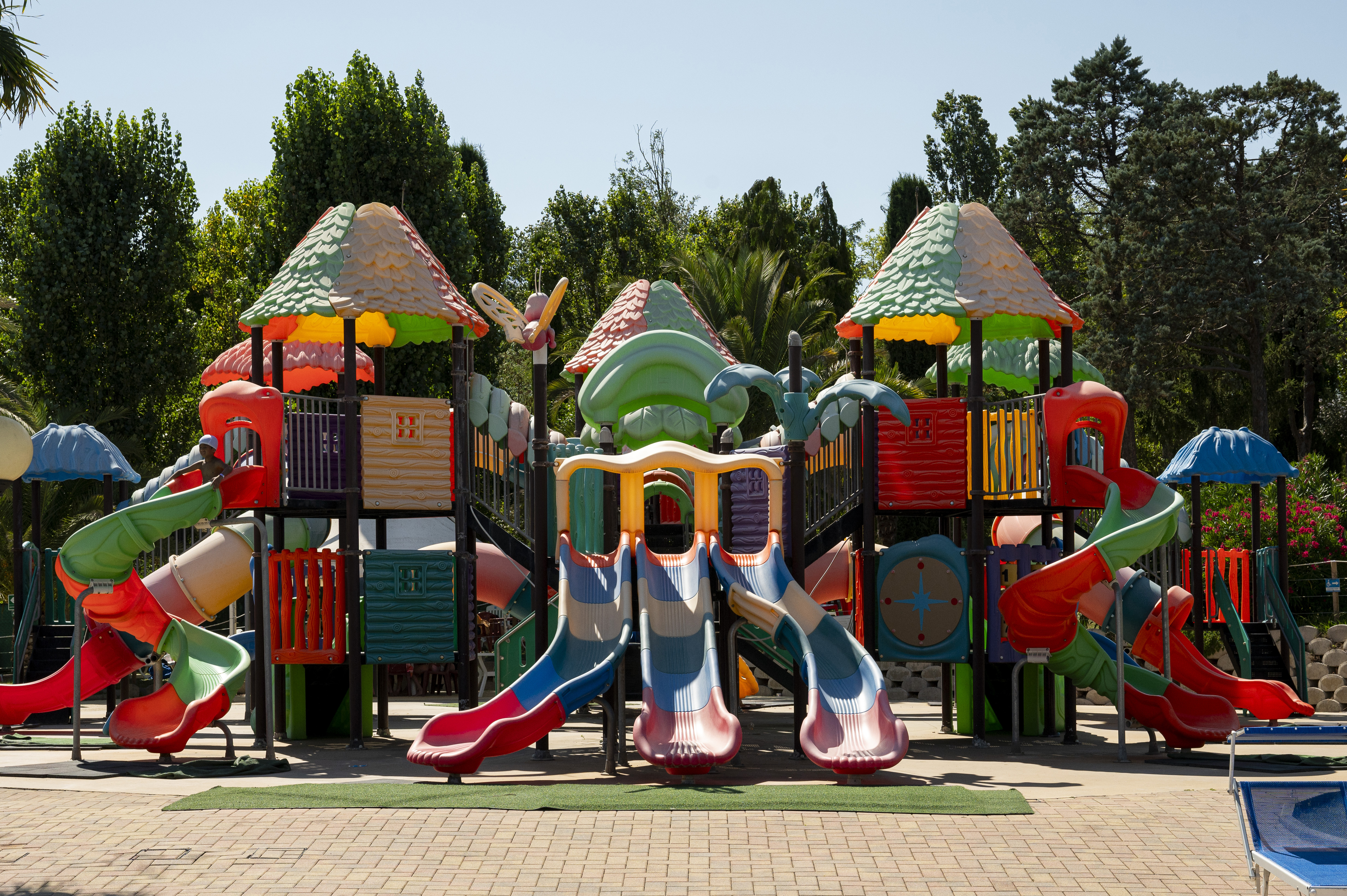 Colorful playground structure with multiple slides and towers, set in a leafy park area at Centro Vacanze Verde Azzurro