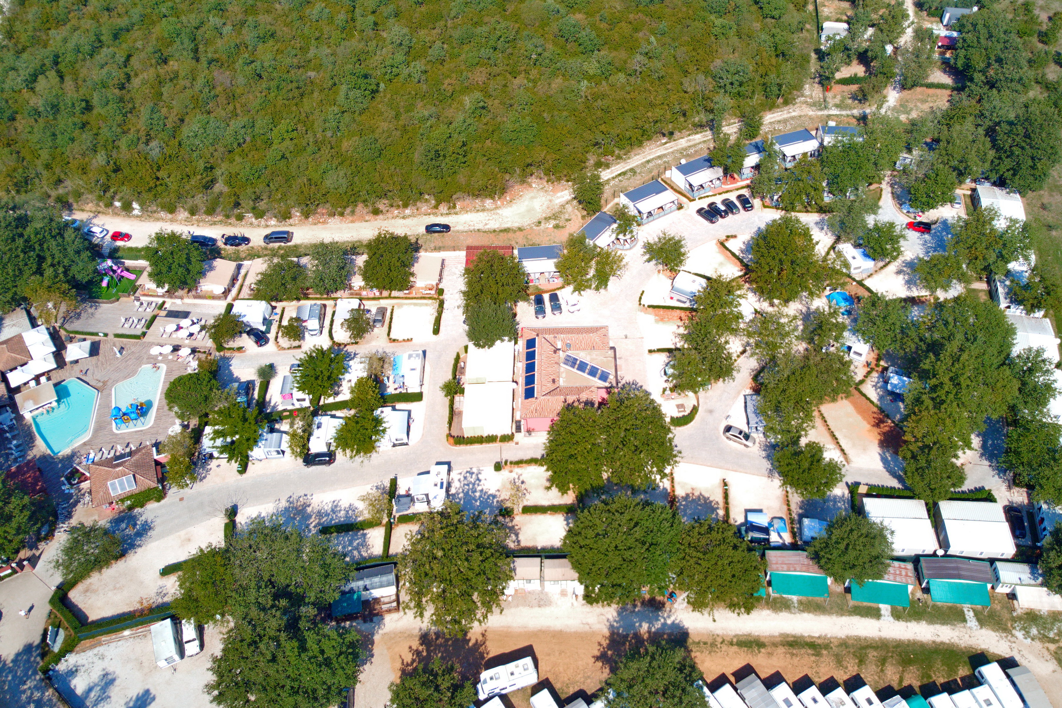 At Polidor, an aerial perspective of the campsite reveals parked RVs, modest structures, and a swimming pool encircled by foliage and lush vegetation.