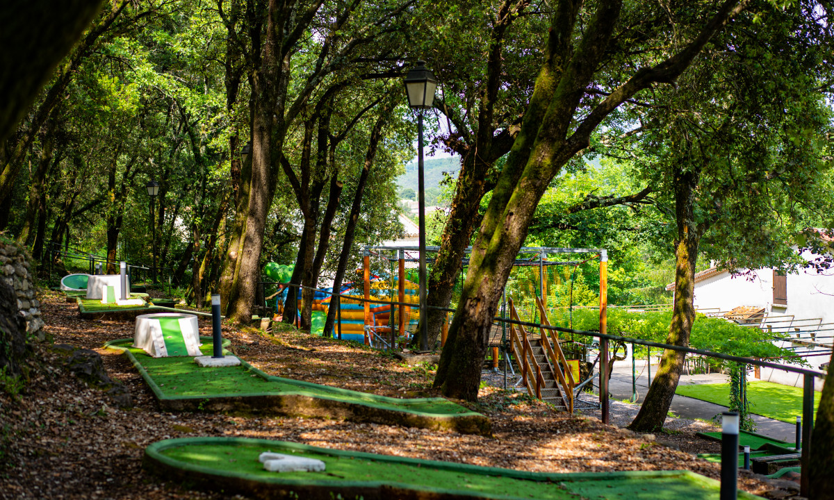 At La Clémentine, there is a mini-golf course nestled beneath trees, encircled by lush vegetation and play structures.