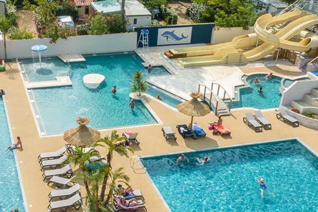 At Les Jardins de Tivoli, swimming pools featuring water slides, loungers, and parasols are filled with individuals swimming and sunbathing.