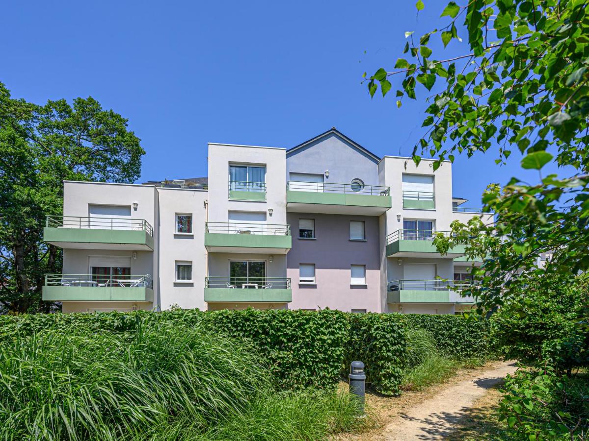A multi-story apartment building with balconies stands amid lush greenery and a clear blue sky at Ker Goh Lenn