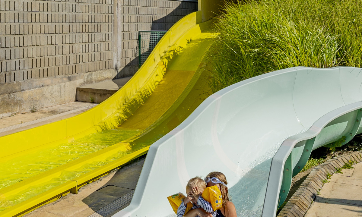 At De la Plage, youngsters are gliding down a curved water slide, encircled by lush greenery and concrete barriers.