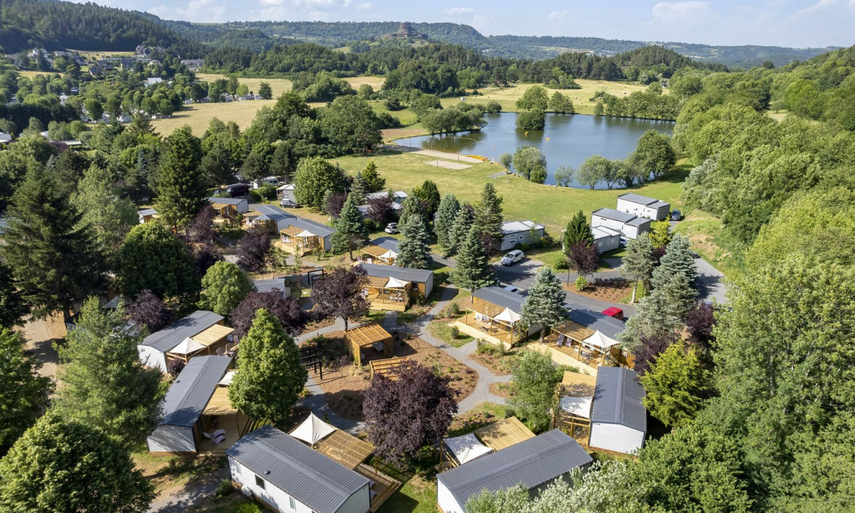 Cabins surrounded by trees, located near a lake with scenic, hilly terrain in the background at La Ribeyre