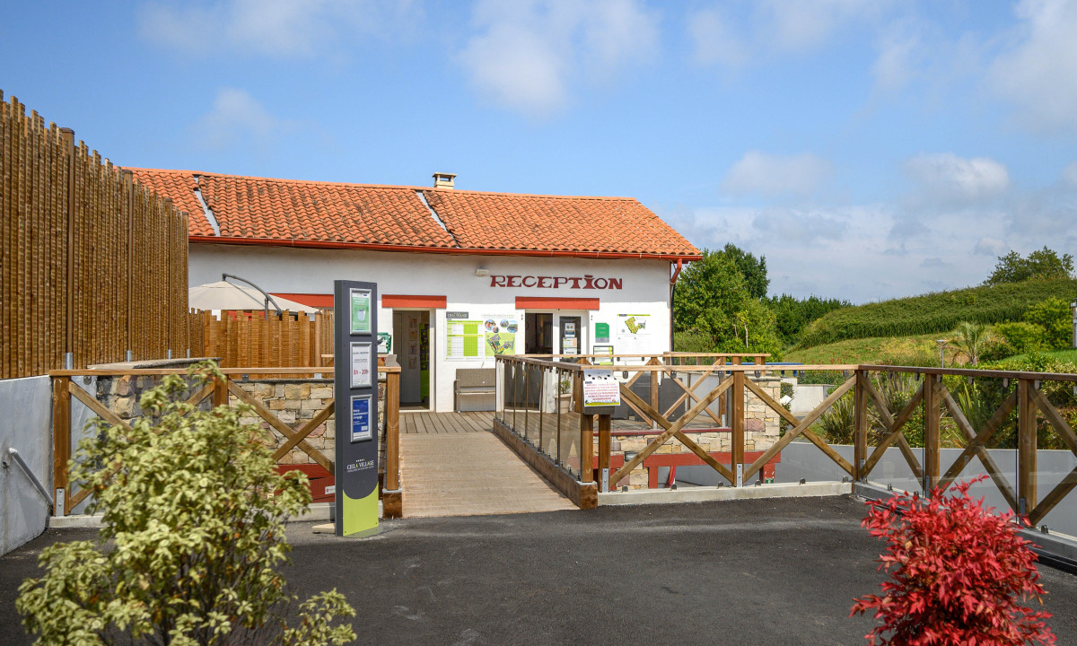 Reception building with red-tiled roof, surrounded by a wooden fence and greenery, under a blue, partly cloudy sky at Atlantica