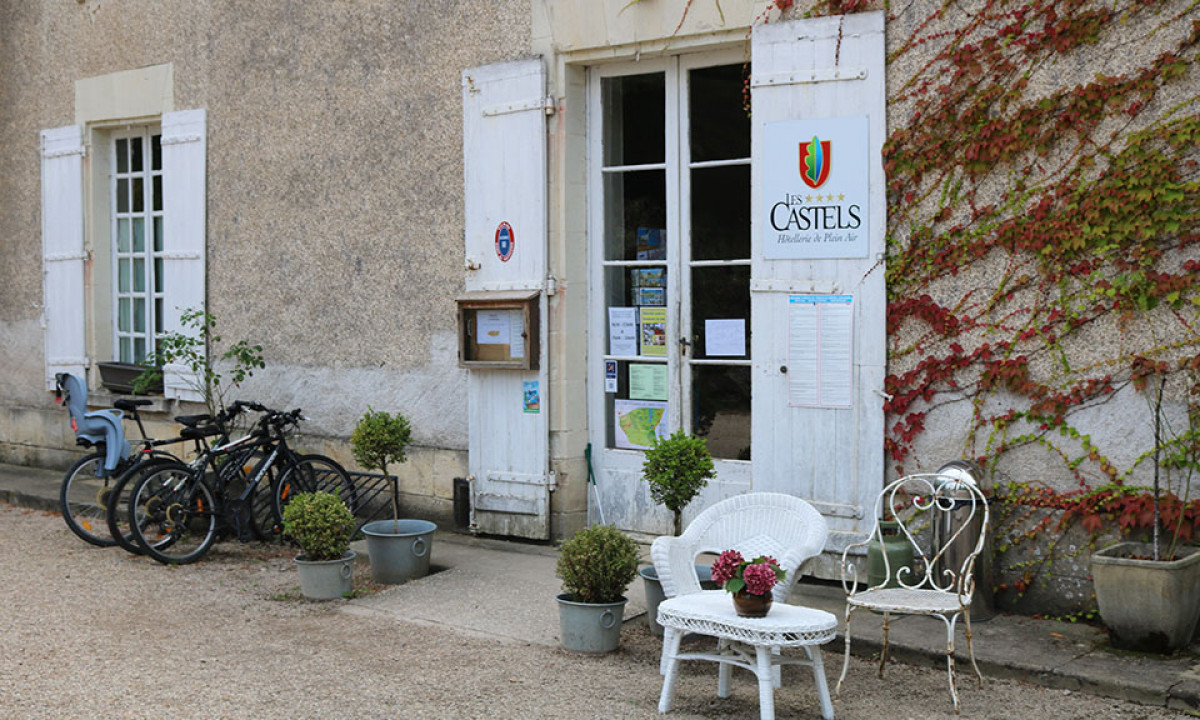 At Le Petit Trianon, white seating and a table are set up outdoors near a charming structure, accompanied by bicycles and potted greenery in the vicinity.
